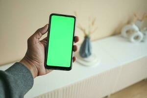 men holding a smart phone with green screen against home interior decoration photo