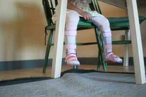 Child cerebral palsy disability with legs orthosis shoes sitting on a chair photo