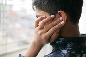 teenage boy having ear pain touching his painful ear , photo