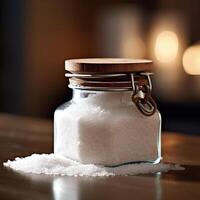 Large sea salt in a glass jar on a wooden table. Blurred brown background. . photo