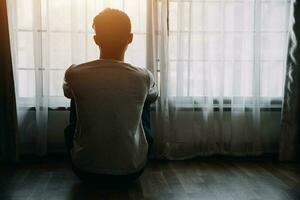 solo hombre silueta curioso a el ventana cerrado con cortinas en dormitorio. hombre soportes a ventana solo foto