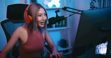 metraggio di giovane asiatico donna influencer indossare cuffie parlando in un' microfono mentre registrazione un' Radio mostrare nel un' vivente camera casa studio a notte con neon luce. soddisfare Creatore concetto. video