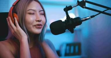 Aufnahmen von jung asiatisch Frau Influencer tragen Kopfhörer reden in ein Mikrofon während Aufzeichnung ein Radio Show im ein Leben Zimmer Zuhause Studio beim Nacht mit Neon- Licht. Inhalt Schöpfer Konzept. video
