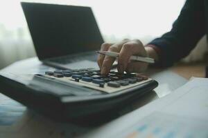 Close up businessman hand using calculator and working with laptop calculate about finance accounting at coffeeshop outdor.finance accounting concept photo