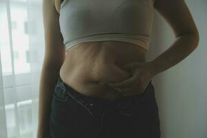 mujer gorda, barriga gorda, gordita, mujer obesa mano sosteniendo grasa abdominal excesiva con cinta métrica, concepto de estilo de vida de dieta de mujer foto