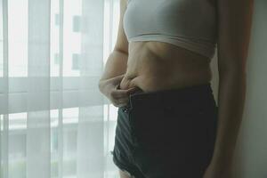 mujer gorda, barriga gorda, gordita, mujer obesa mano sosteniendo grasa abdominal excesiva con cinta métrica, concepto de estilo de vida de dieta de mujer foto