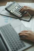 Close up woman hand using calculator and writing make note with calculate about cost at home office. photo