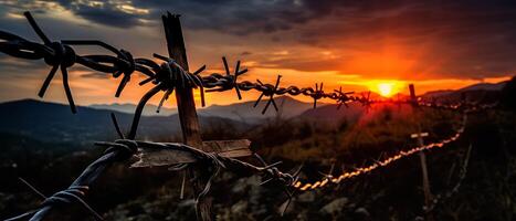 A barbed wire fence with a view of the sunset in the distance. . photo