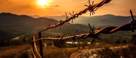 A barbed wire fence with a view of the sunset in the distance. . photo