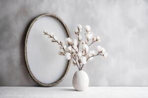 Front view product photo of white oval frame with wild Cotton branches in glass vase behind the frame.