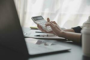 Asian Business woman using calculator and laptop for doing math finance on an office desk, tax, report, accounting, statistics, and analytical research concept photo