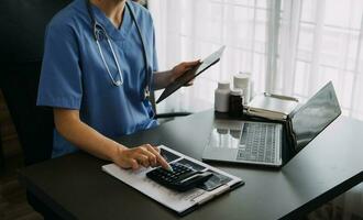 Doctor working with laptop computer and writing on paperwork. Hospital background. photo