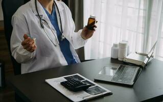 Doctor working with laptop computer and writing on paperwork. Hospital background. photo