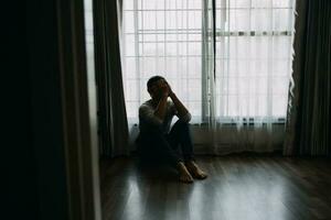 solo hombre silueta curioso a el ventana cerrado con cortinas en dormitorio. hombre soportes a ventana solo foto