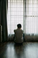 solo hombre silueta curioso a el ventana cerrado con cortinas en dormitorio. hombre soportes a ventana solo foto