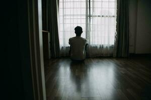 solo hombre silueta curioso a el ventana cerrado con cortinas en dormitorio. hombre soportes a ventana solo foto