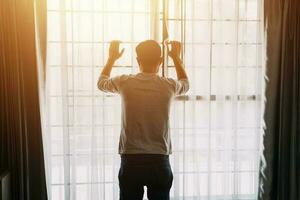 Alone man silhouette staring at the window closed with curtains in bedroom. Man stands at window alone photo