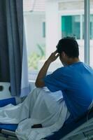 young injured man in hospital room sitting alone in pain looking negative and worried for his bad health condition sitting on chair suffering depression on a sad lonely medical background photo