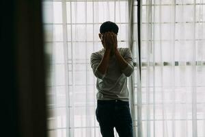 Alone man silhouette staring at the window closed with curtains in bedroom. Man stands at window alone photo