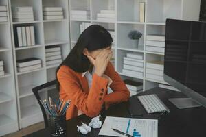 Asian women sitting in a home office With stress and eye strain.Tired businesswoman holding eyeglasses and massaging nose bridge. There are tablets, laptops, and coffee. photo