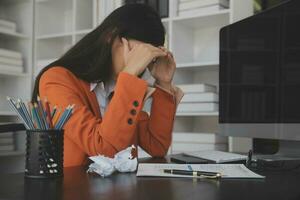 Asian women sitting in a home office With stress and eye strain.Tired businesswoman holding eyeglasses and massaging nose bridge. There are tablets, laptops, and coffee. photo