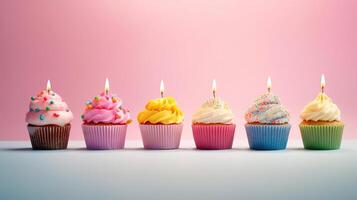 Row of colorful birthday cupcakes with candle of each, on light pink background. photo