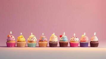 Row of colorful birthday cupcakes with candle of each, on light pink background. photo