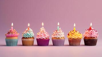 Row of colorful birthday cupcakes with candle of each, on light pink background. photo