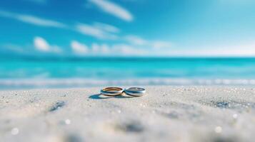 Pair wedding rings standing in sand on tropical beach with blur blue sea and blue sky. photo