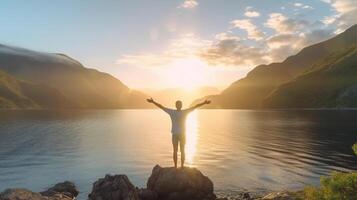Young man arms outstretched by the sea at sunrise with sea and mountain view. photo