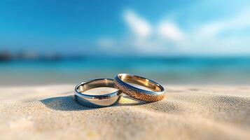 Pair wedding rings standing in sand on tropical beach with blur blue sea and blue sky. photo