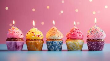 Row of colorful birthday cupcakes with candle of each, on light pink background. photo