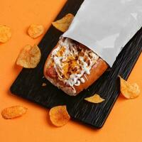 hot dog with cheese and chips on a black plate on an orange background photo