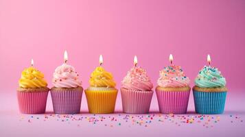 Row of colorful birthday cupcakes with candle of each, on light pink background. photo