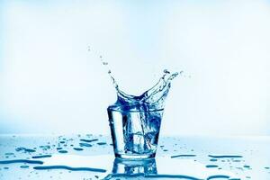 Ice that fell into the glass with water splashing from glass isolated on blue background photo