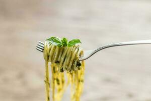 Spaghetti with pesto sauce and basil leaf on the fork photo