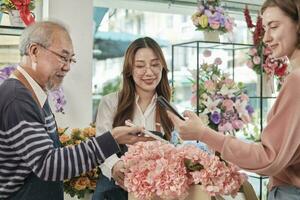 Florist workers team delivering fresh blossoms to white customer who purchased order, cashless payment by smartphone application, happy work in colorful flower shop, small business SME entrepreneur. photo