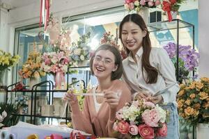 Portrait of two cheerful young beautiful female florist partners team smile and look at camera with bloom bouquet happy work in colorful flower shop store with fresh flora, SME business entrepreneur. photo