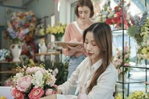 dos joven hermosa hembra florista socios trabajando con manojo de flores acuerdo, decorando con encantador florido, compra orden trabajo en vistoso flor tienda almacenar, SME negocio emprendedor. foto