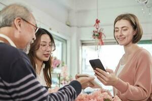 Florist workers team delivering fresh blossoms to white customer who purchased order, cashless payment by smartphone application, happy work in colorful flower shop, small business SME entrepreneur. photo