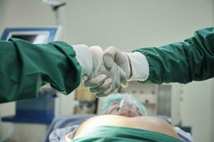 Close up, two specialist surgeon doctors shake hands with gloves after surgery operations success on critical patient in hospital's ICU, professional medical team cooperates. photo