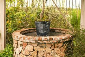 Vintage stone brick well with black steel bucket in garden photo