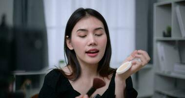 Handheld shot, Beautiful asian woman blogger is showing how to makeup and use cosmetics. In front of the smartphone to record vlog video live streaming at home. Influencer and cosmetics concepts.