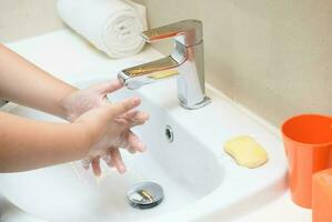 Washing hands child rinsing soap with running water at sink, photo