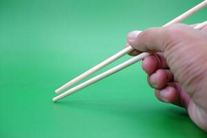 hand holding a pair of chopsticks isolated on green background. photo