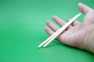 hand holding a pair of chopsticks isolated on green background. photo