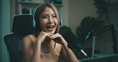 Footage of Young Asian woman influencer wearing headphones talking into a microphone while recording a radio show in a living room home studio. Content creator and influencer marketing concepts. video