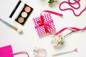 hembra lugar de trabajo de un Moda blogger productos cosméticos, un regalo caja con un arco. plano laico en un blanco antecedentes foto