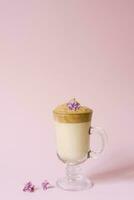 Beautiful dalgon coffee drink. Coffee mug in clear glass with foam and lilac flower on a lilac pink background. photo