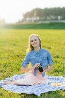 sonriente joven mujer usos un cámara a tomar un imagen en el parque en el verano foto
